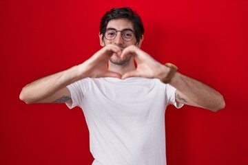 Canvas Print - Young hispanic man standing over red background smiling in love doing heart symbol shape with hands. romantic concept.