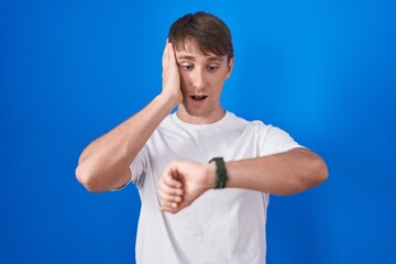 Sticker - Caucasian blond man standing over blue background looking at the watch time worried, afraid of getting late