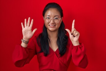 Wall Mural - Asian young woman standing over red background showing and pointing up with fingers number seven while smiling confident and happy.