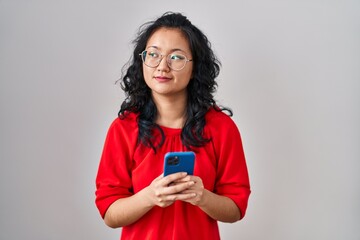 Canvas Print - Young asian woman using smartphone typing message smiling looking to the side and staring away thinking.