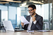 © Liubomir - Arab investor financier, holding hand up winner triumphant gesture, businessman at workplace inside office paper work, looking at reports, satisfied with results of financial success achievement.