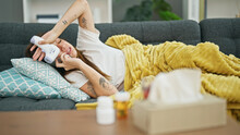 Young Beautiful Hispanic Woman Lying On The Sofa Sick Talking On Smartphone Holding Thermometer At Home