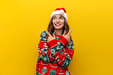 Unsure Girl In Christmas Sweater And Santa Claus Hat Chooses From Two Options On Yellow Isolated Background