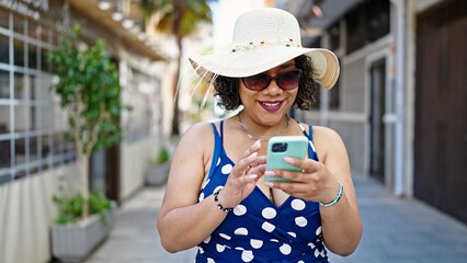 Canvas Print - Young beautiful latin woman tourist wearing summer hat and sunglasses using smartphone at street