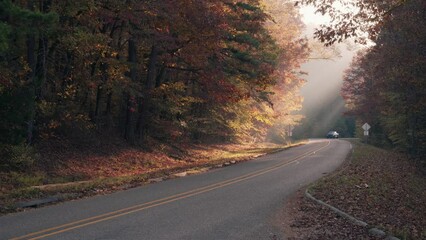 Wall Mural - A gray pickup truck drives a country mountain road in fall through an autumn forest with light rays 