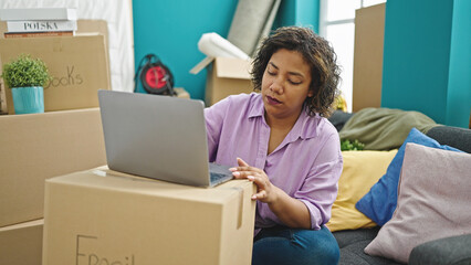 Canvas Print - Young beautiful latin woman using laptop sitting on sofa at new home