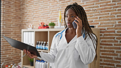 Canvas Print - African american woman doctor talking on smartphone holding medical report at the clinic