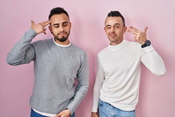 Poster - Homosexual couple standing over pink background shooting and killing oneself pointing hand and fingers to head like gun, suicide gesture.