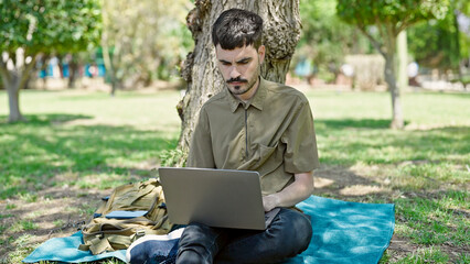 Wall Mural - Young hispanic man using laptop sitting on floor at park