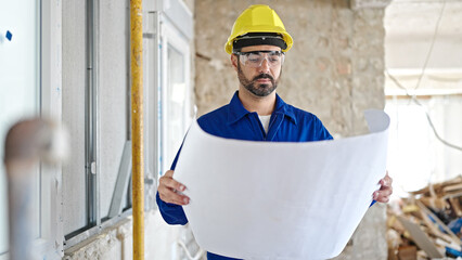 Canvas Print - Young hispanic man worker wearing hardhat reading house project at construction site