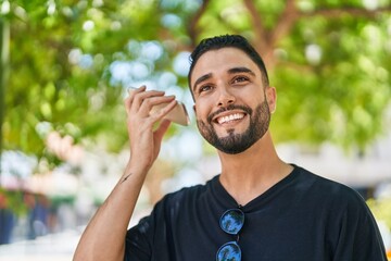 Wall Mural - Young arab man miling confident listening audio message by the smartphone at park