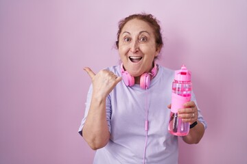 Poster - Senior woman wearing sportswear and headphones surprised pointing with hand finger to the side, open mouth amazed expression.