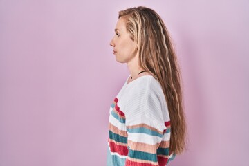 Sticker - Young blonde woman standing over pink background looking to side, relax profile pose with natural face and confident smile.