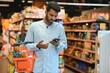 © Serhii - Young man using mobile phone while shopping at supermarket