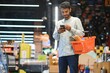 © Serhii - Young man using mobile phone while shopping at supermarket