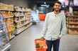 Portrait of happy Indian man standing in front of the product counter in a grocery store. Man buying grocery for home in supermarket.