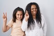 © Krakenimages.com - Mother and young daughter standing over white background smiling looking to the camera showing fingers doing victory sign. number two.