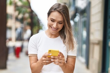 Wall Mural - Young caucasian woman smiling confident using smartphone at street