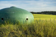 Stalowa kopuła bunkra pomalowana na zielono wpasowująca się idealnie w rolniczy krajobraz okolicy