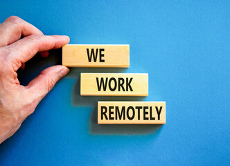 We work remotely symbol. Concept words We work remotely on wooden block. Beautiful blue table blue background. Businessman hand. Business we work remotely concept. Copy space.