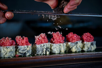 Wall Mural - Crop person grating truffle on delicious uramaki sushi rolls with raw tuna