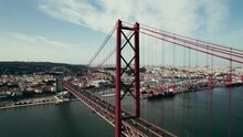 A Drone Flies Over A Red Suspension Car Bridge On A Summer Day. Panoramic View Of The City On The River Bank, Bird's-eye View
