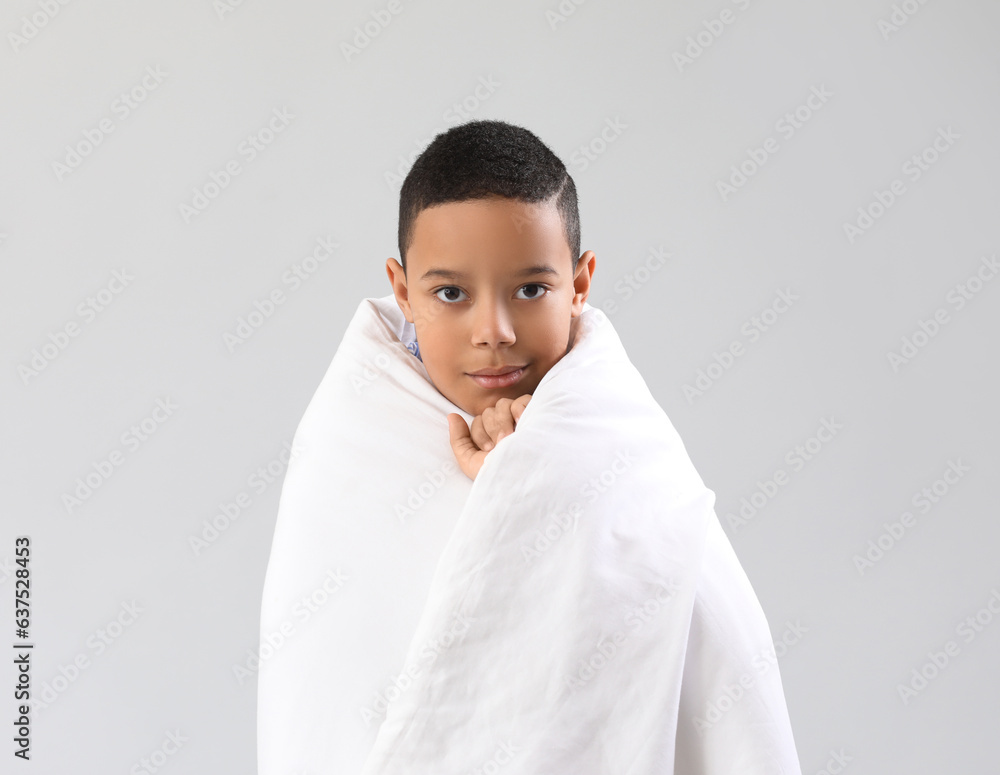 Little African-American boy with soft blanket on light background