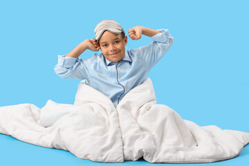 Wall Mural - Little African-American boy with sleeping mask and soft blanket on blue background