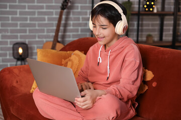 Wall Mural - Little boy with headphones using laptop at home late in evening