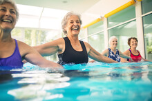 Elderly Happy Women Do Aqua Aerobics In The Indoor Pool. Women Look At The Instructor And Repeat The Exercises