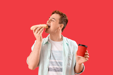 Poster - Young man with tasty hot dog and cup of coffee on red background