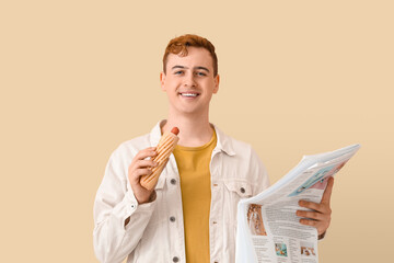 Canvas Print - Young man with tasty hot dog and newspaper on beige background