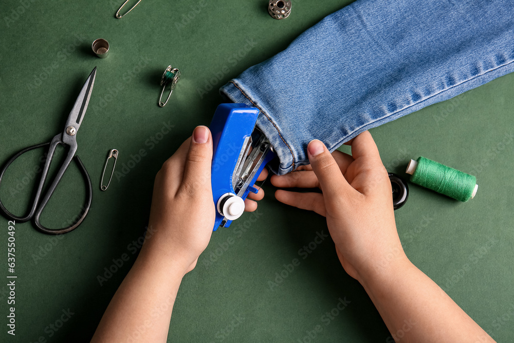 Female hands with different supplies sewing jeans on green background