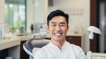 Portrait Of A Smiling Asian Man Sitting In The Dentist's Office. Laughing Chinese Guy With Perfect Teeth Waiting In A Doctor's Cabinet. Cheerful Handsome Young Japanese Man, Dental Treatment