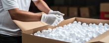 A Worker Is Carefully Packing A Fragile Item In Styrofoam Peanuts Before Placing It Inside The Shipping Box.