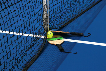 Wall Mural - Side view of two pickleball paddles and one yellow whiffle ball on a blue court