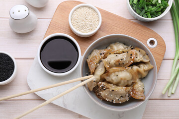 Delicious gyoza (asian dumplings), soy sauce and sesame on white wooden table, flat lay