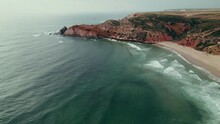 Bird's-eye View Of The Seashore With A Cliff Covered With Green Grass At The Top, A Narrow Strip Of Sandy Beach At The Foot Of The Mountain, Drone Video