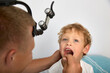 Experienced ENT doctor carefully examines palatine tonsils of child for presence of disease. Using a wooden spatula for the throat, the otolaryngologist checks the condition of the child's oral cavity