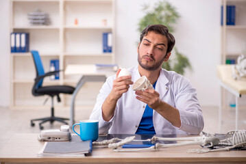 Wall Mural - Young male doctor studying human skeleton at the hospital