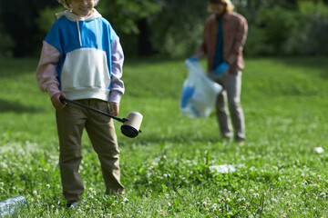 Wall Mural - Closeup of little boy picking up trash in nature eco activist family, copy space