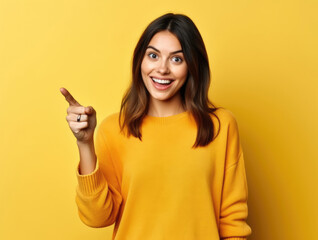 A young woman on a yellow background smiles and points her finger at something