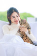 © Bangkok Click Studio - Asian young pretty female teenager girl in turtleneck sweater laying lying down on cozy comfortable white clean sheet bed under blanket smiling playing holding little cute cats.