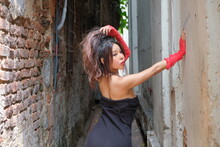 Asian Woman Stands In A Small Alley One Hand On A Wall, The Other In Her Hair