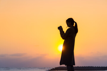 Wall Mural - Silhouette of woman use camera to take photo at sunset in the beach