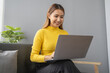 © kamiphotos - Asian woman relaxing at living room, young businesswoman spends her vacation watching movies, listening to music and surfing social media on laptop, texting and chatting with friends. Weekend concept.