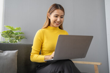 Asian woman relaxing at living room, young businesswoman spends her vacation watching movies, listening to music and surfing social media on laptop, texting and chatting with friends. Weekend concept.