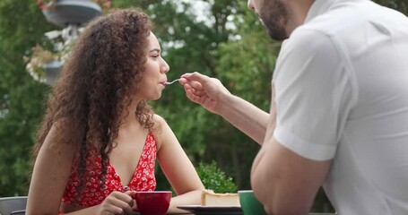 Poster - Happy couple spending time together at outdoor cafe. Man feeding his girlfriend with tasty cheesecake, love angle view