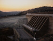 Oroville Dam at sunset, showing the massive outflow mechanism, and a road that passes by it. The dam is a major part of California's water infrastructure.