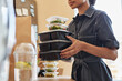 © Seventyfour - Close up of young African American woman unpacking food delivery order at home and holding stack of containers